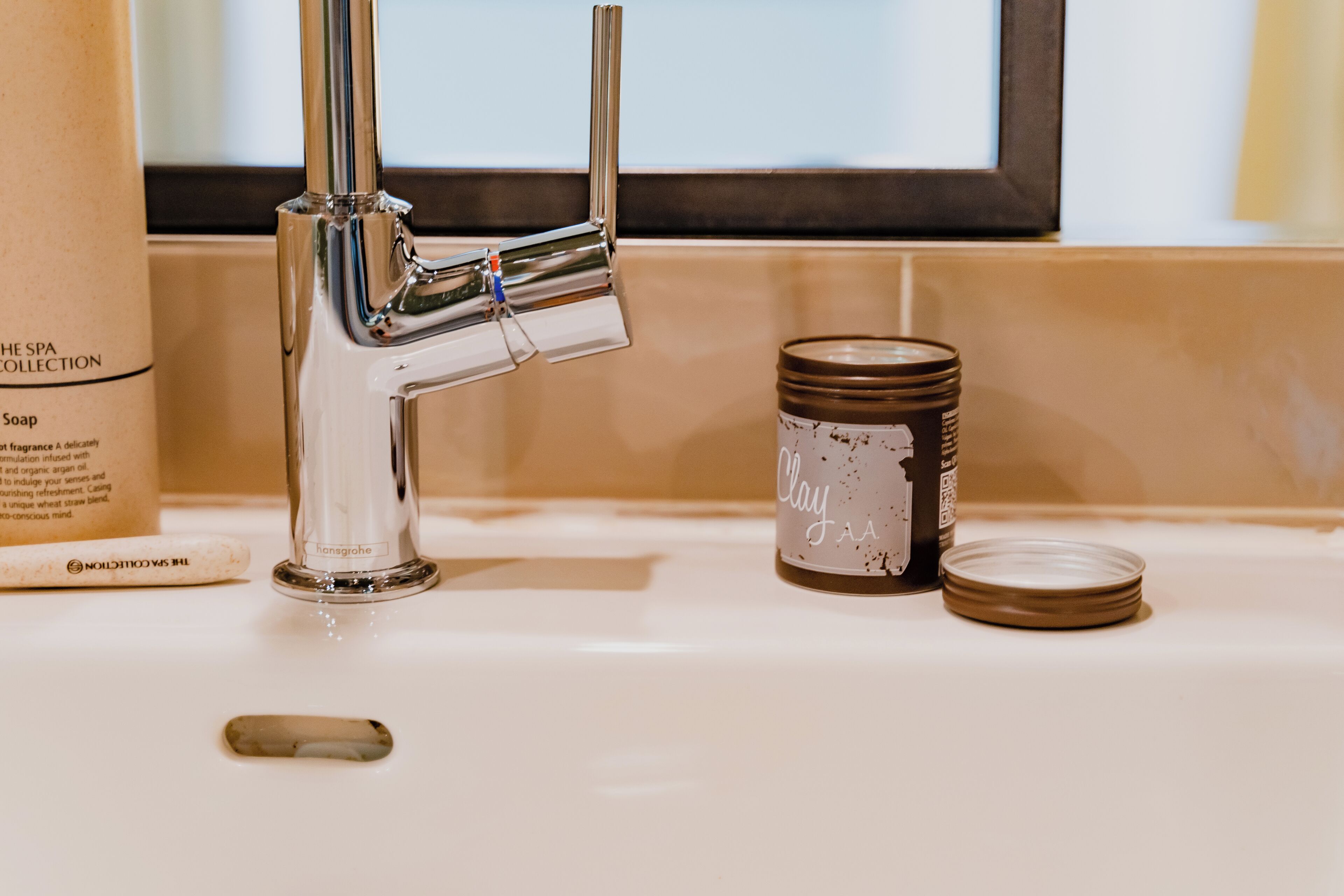 A bathroom sink with a chrome faucet, a soap dispenser, and a candle.