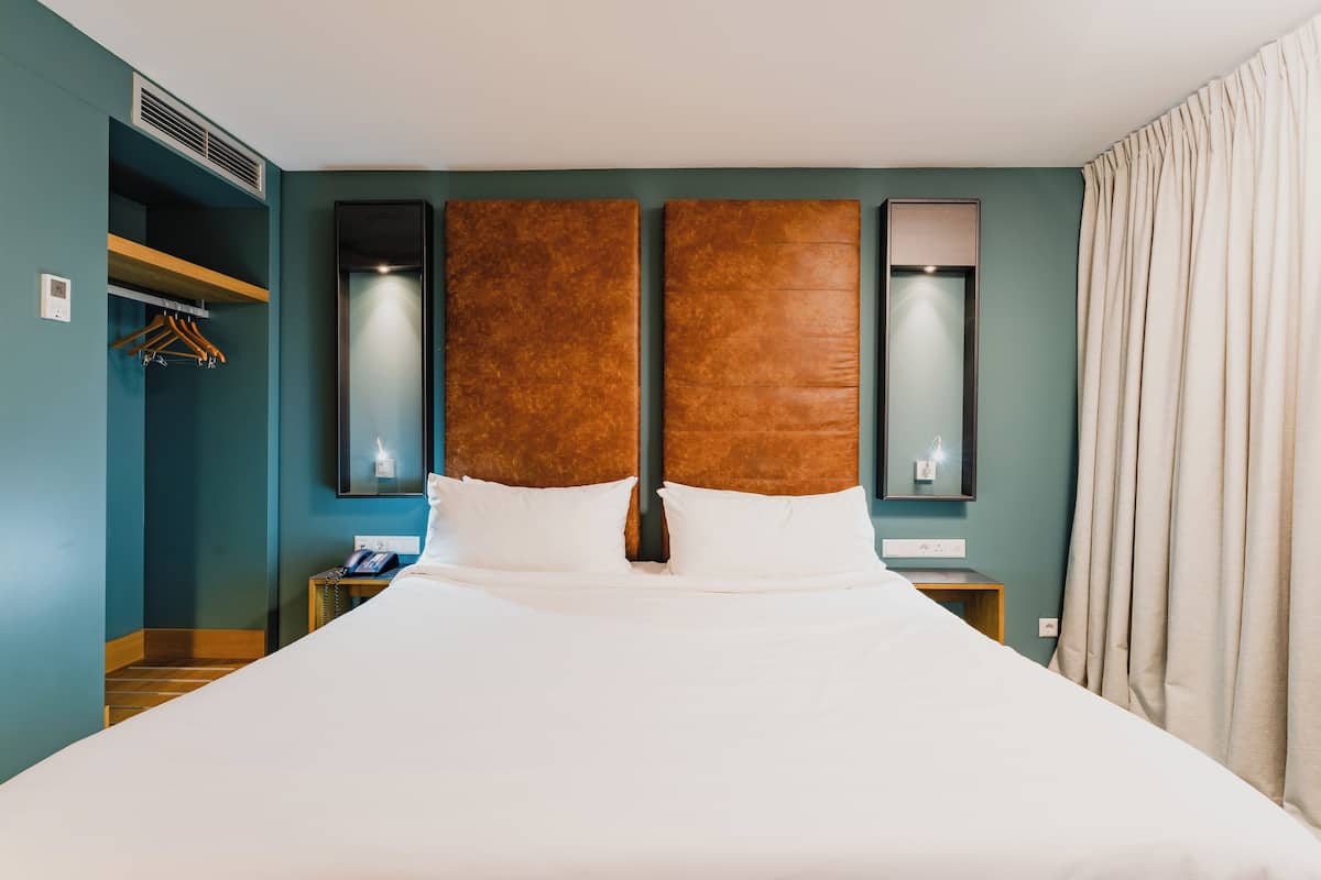 A hotel room with a large bed, a wooden shelf, a mirror, and a nightstand.