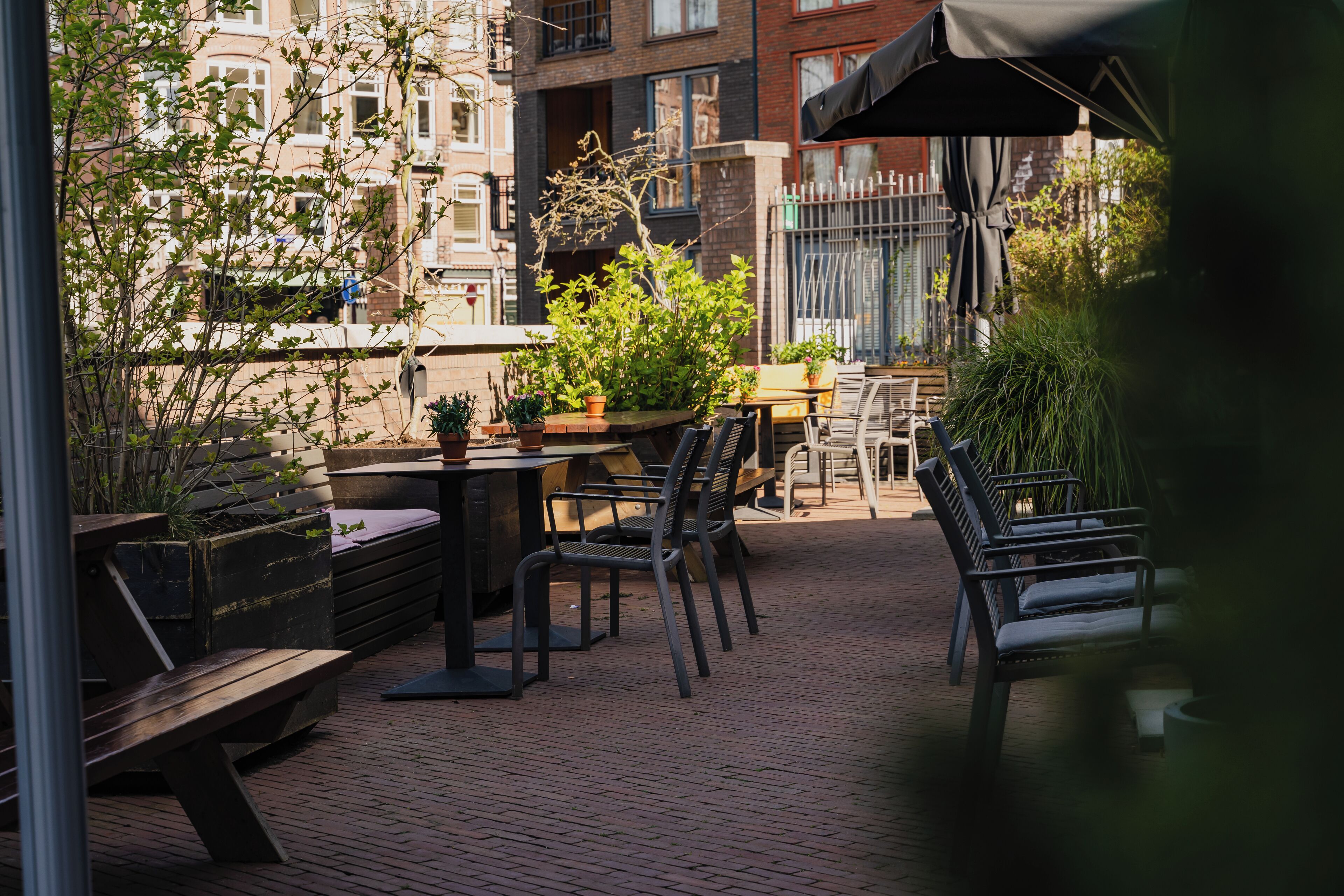 An outdoor patio with brick flooring, metal chairs, tables, and potted plants.