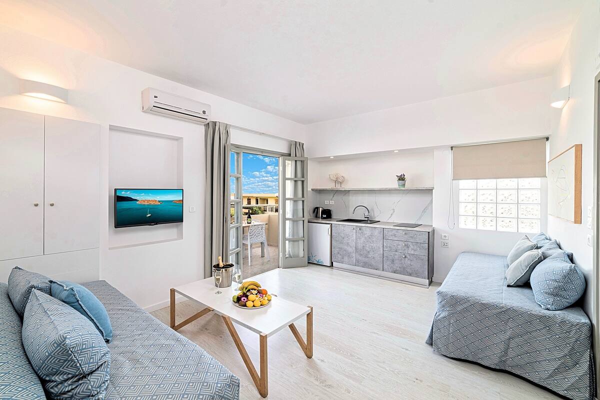 Een moderne woonkamer met een bank, een bijzettafeltje met fruit en een televisie aan de muur.