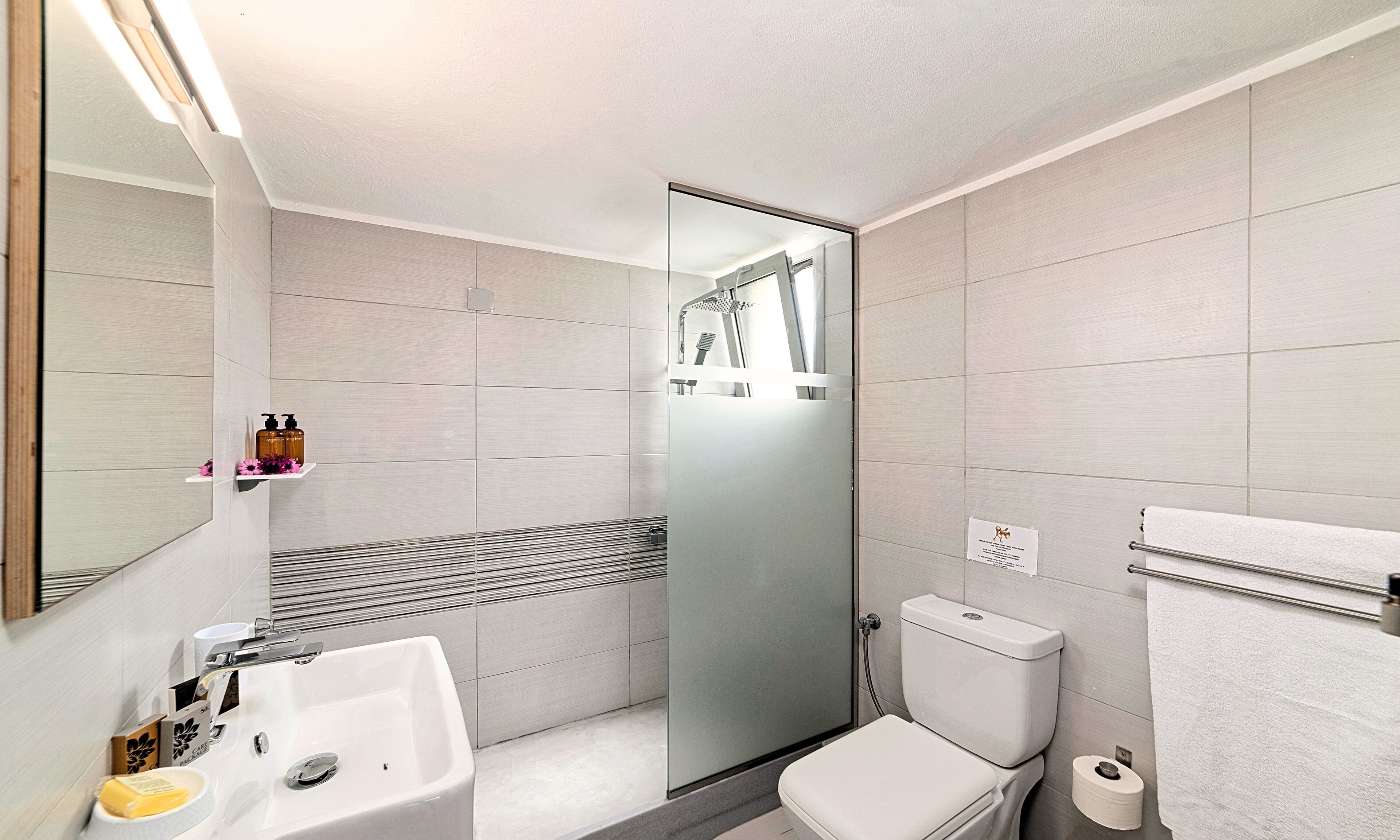 Un baño moderno con cabina de ducha de vidrio, un lavabo blanco y un inodoro.