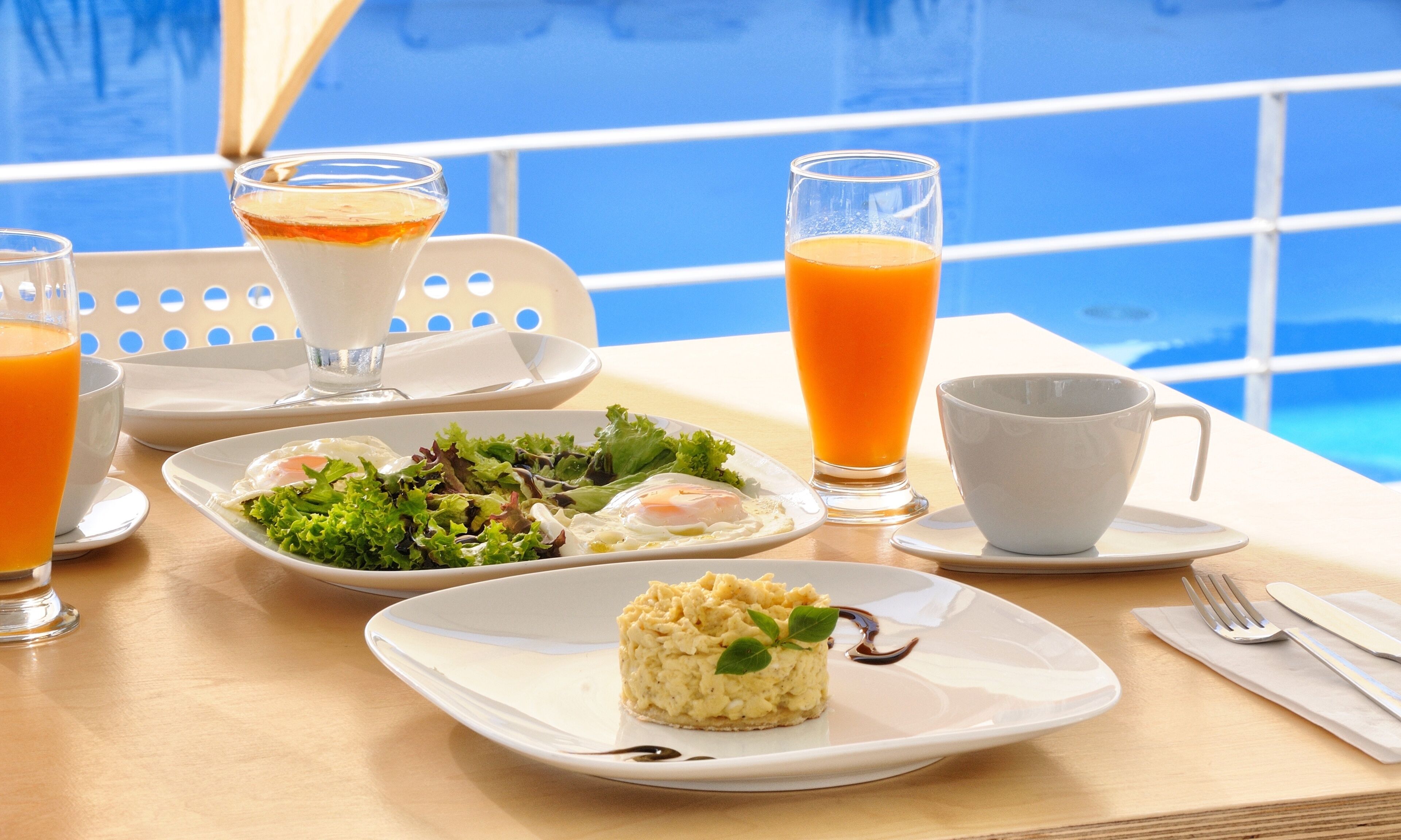 A breakfast table with a salad, eggs, and a dessert, along with glasses of orange juice and a coffee cup.