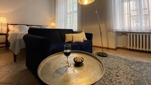 Et hyggeligt rum med en mørkeblå sofa, et rundt bord med et glas vin og en gulvlampe.
