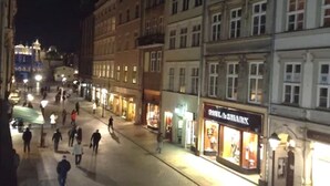 Et natteliv med fodgængere, oplyste butiksvinduer og historiske bygninger.