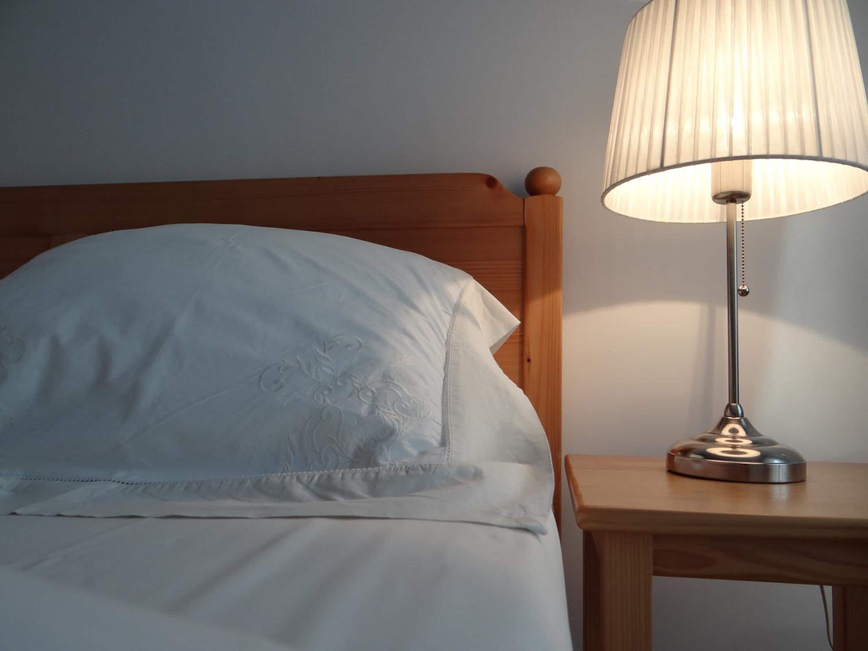 Una cama bien hecha con cabecera de madera y mesita de noche con lámpara.