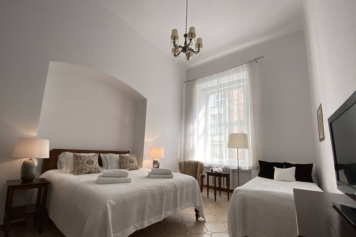 Une chambre d’hôtel avec deux lits, un lustre, une télévision et une fenêtre avec des rideaux.