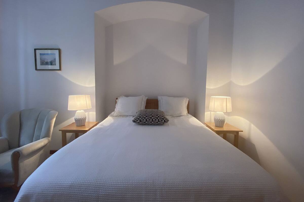Une chambre d’hôtel avec un grand lit, deux tables de chevet avec des lampes, une chaise et un tableau encadré au mur.