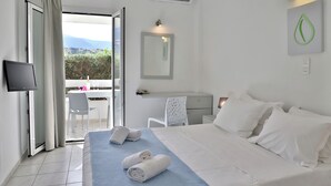 Habitación de hotel con cama, escritorio, silla, televisión y balcón con vistas.