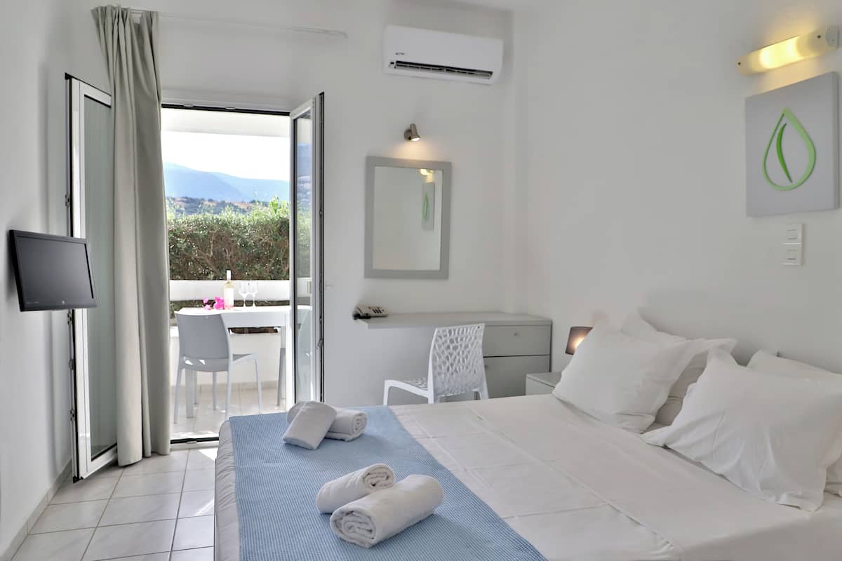 A hotel room with a bed, a desk, a chair, a TV, and a balcony with a view.