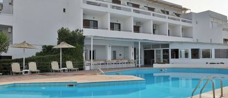 A modern hotel with a swimming pool, outdoor seating, and a covered terrace.