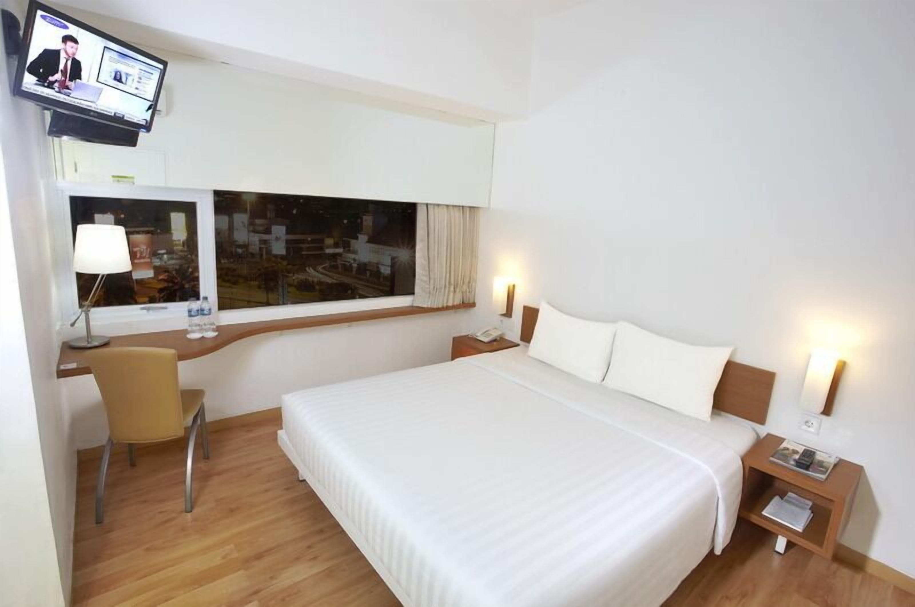 Une chambre d’hôtel avec un grand lit, un bureau avec une chaise, un téléviseur fixé au mur et une fenêtre donnant sur la ville.