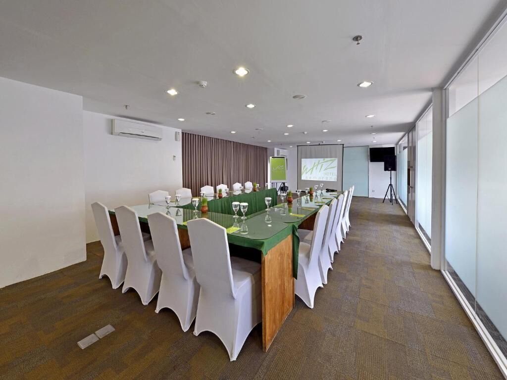 A conference room with a long table, white chairs, and a projector screen.