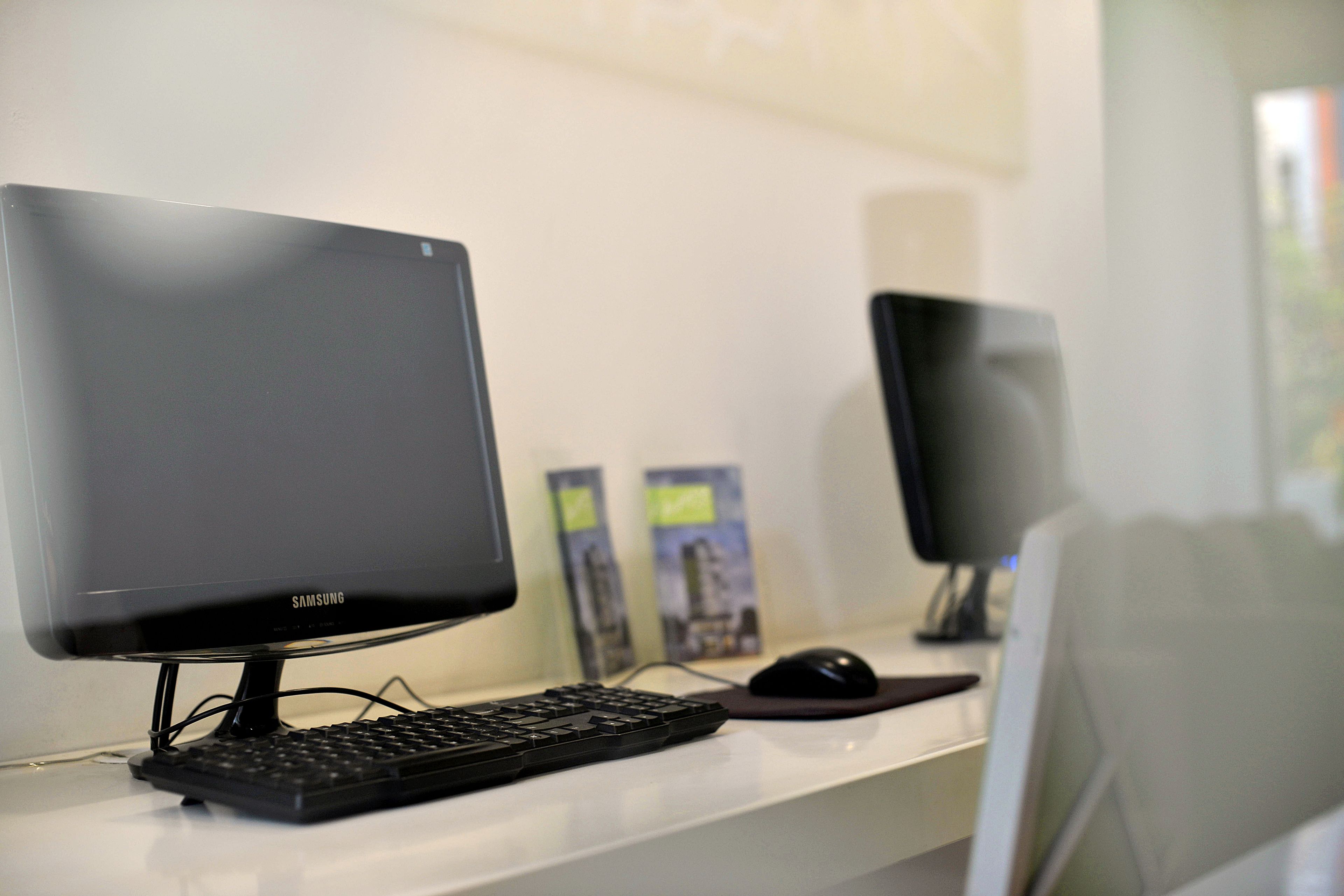 Un écran Samsung posé sur un bureau, avec un clavier et une souris, un haut-parleur et deux affiches accrochées au mur.