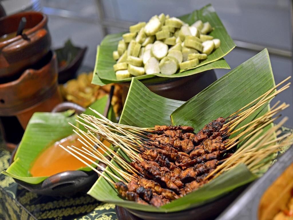 A food display with skewered meats and sliced vegetables on banana leaves, accompanied by clay pots.