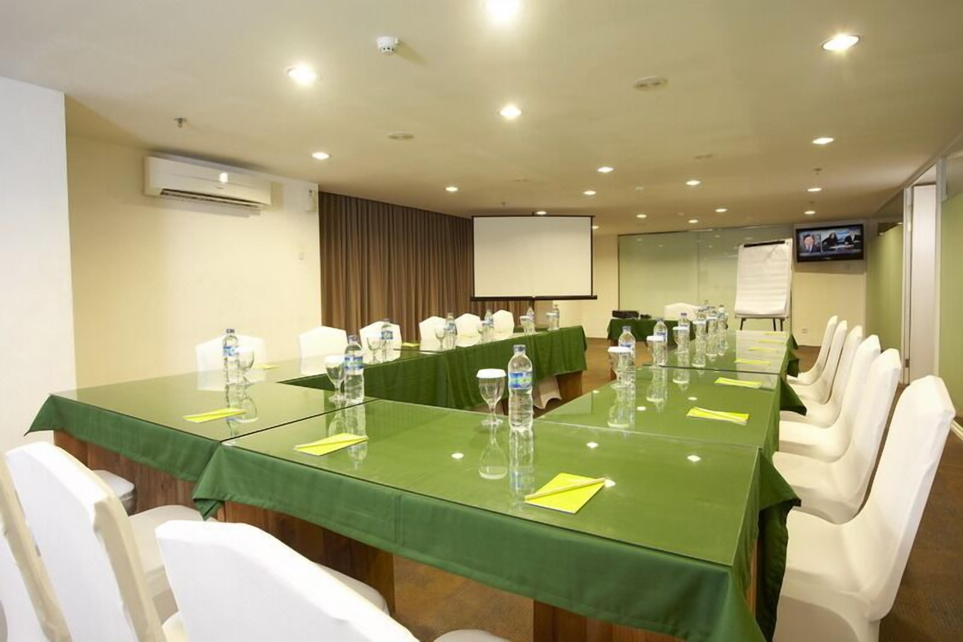 A conference room with a long table, white chairs, and a projector screen.