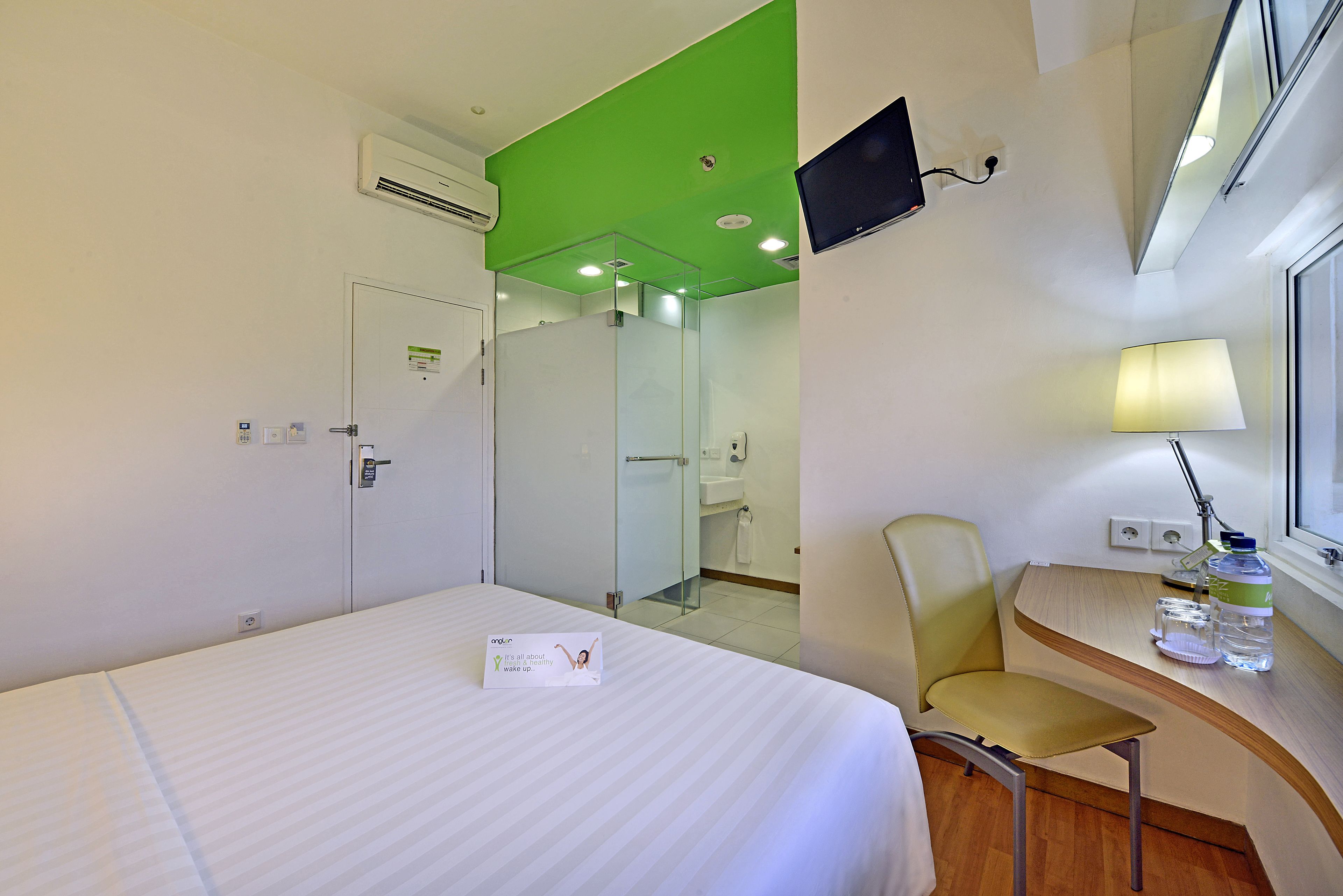 A hotel room with a bed, a chair, a desk with a lamp, a TV, and a window.