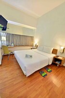 A hotel room with a bed, a desk, a chair, a TV, and slippers on the floor.
