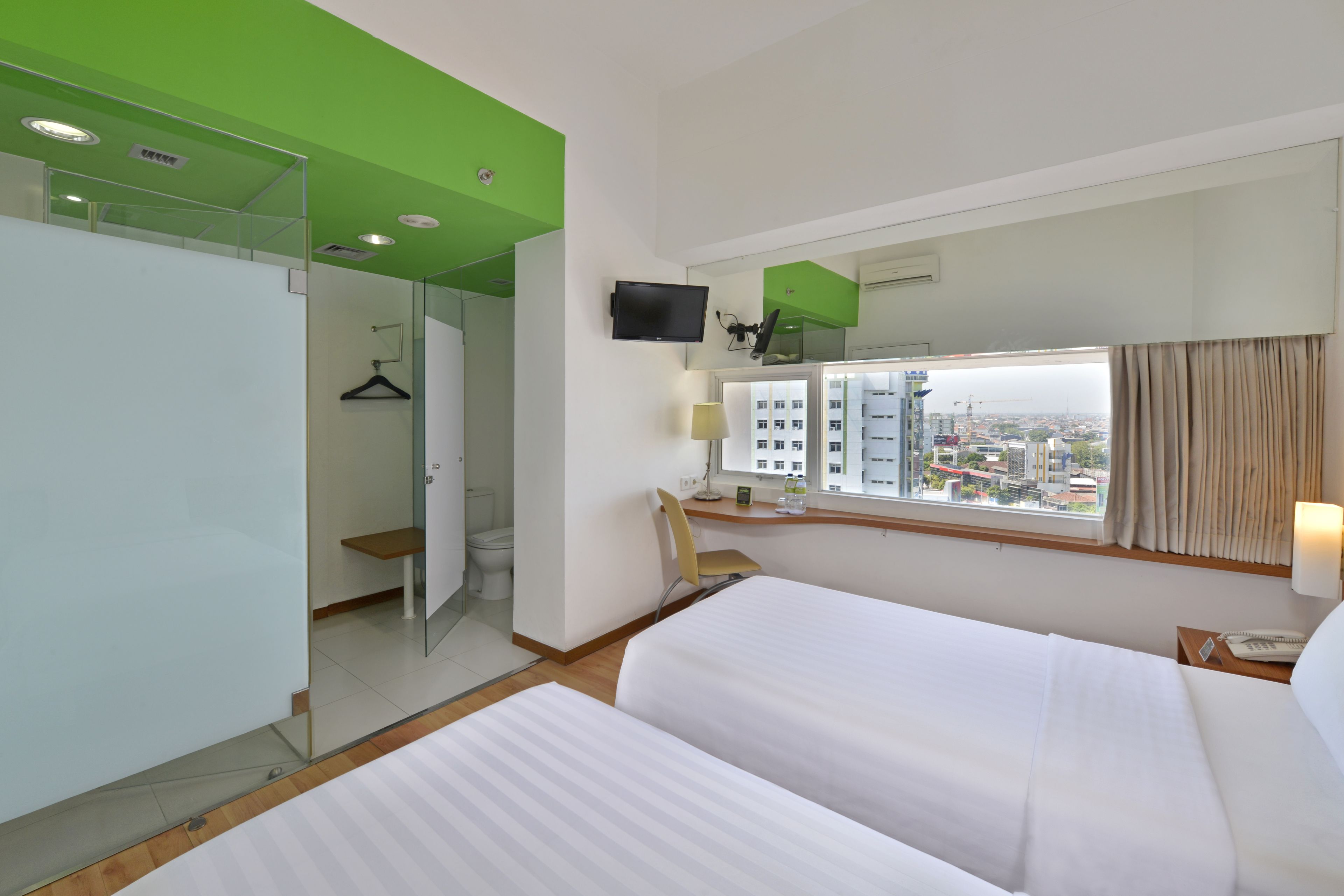A hotel room with two beds, a TV, a window with a city view, and a bathroom with a shower and toilet.