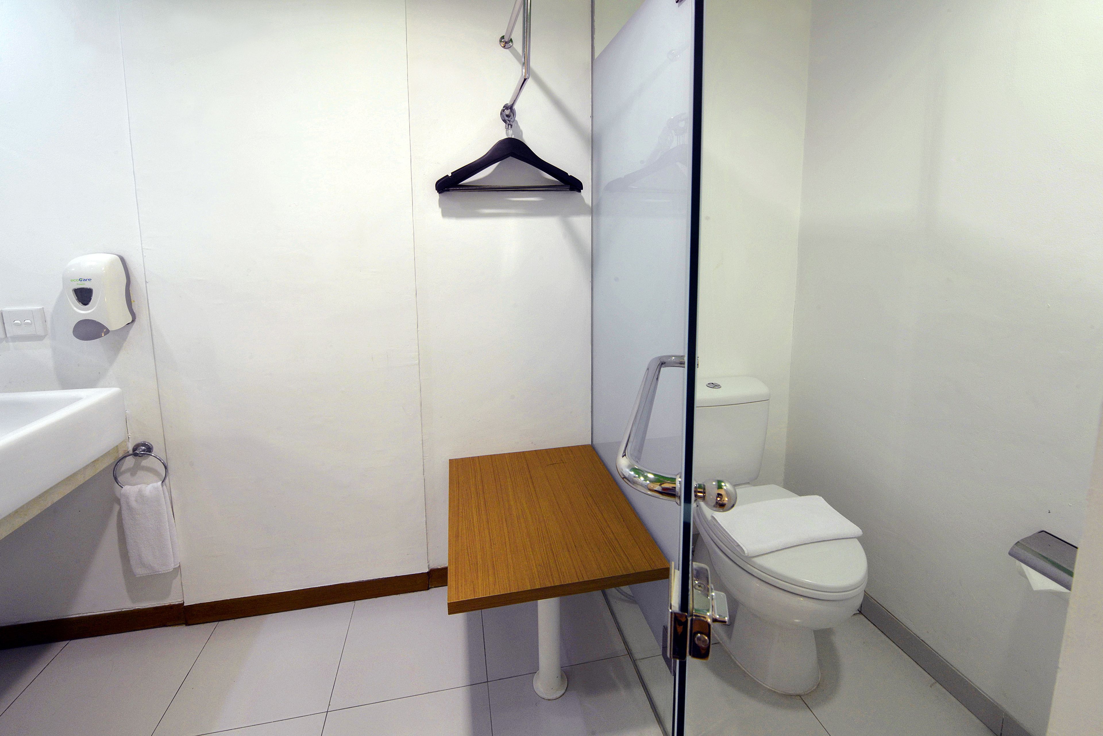 Un baño moderno con un lavamanos blanco, un estante de madera, un toallero colgante y un inodoro.