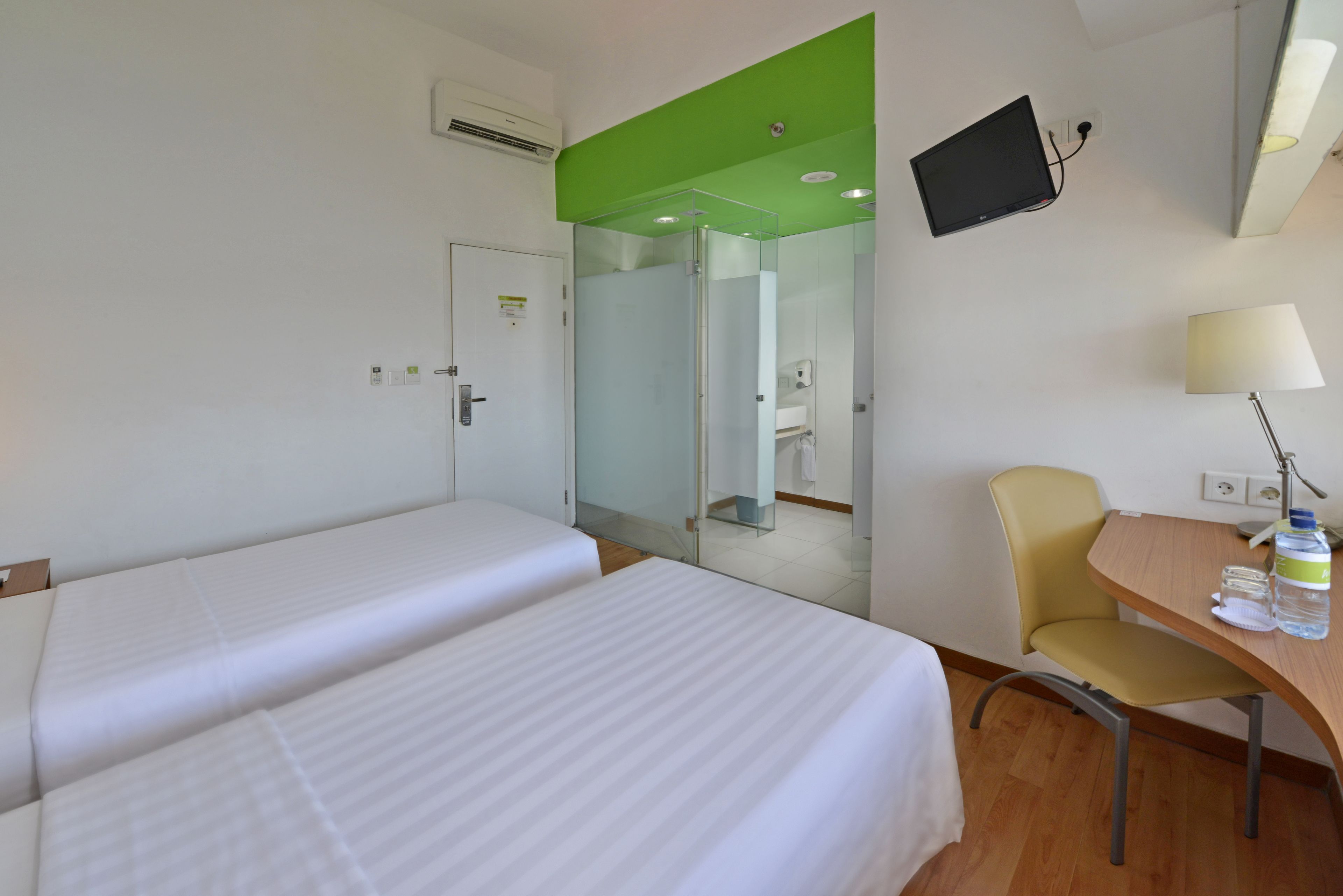 Een hotelkamer met twee bedden, een bureau met stoel, een televisie en een spiegel.