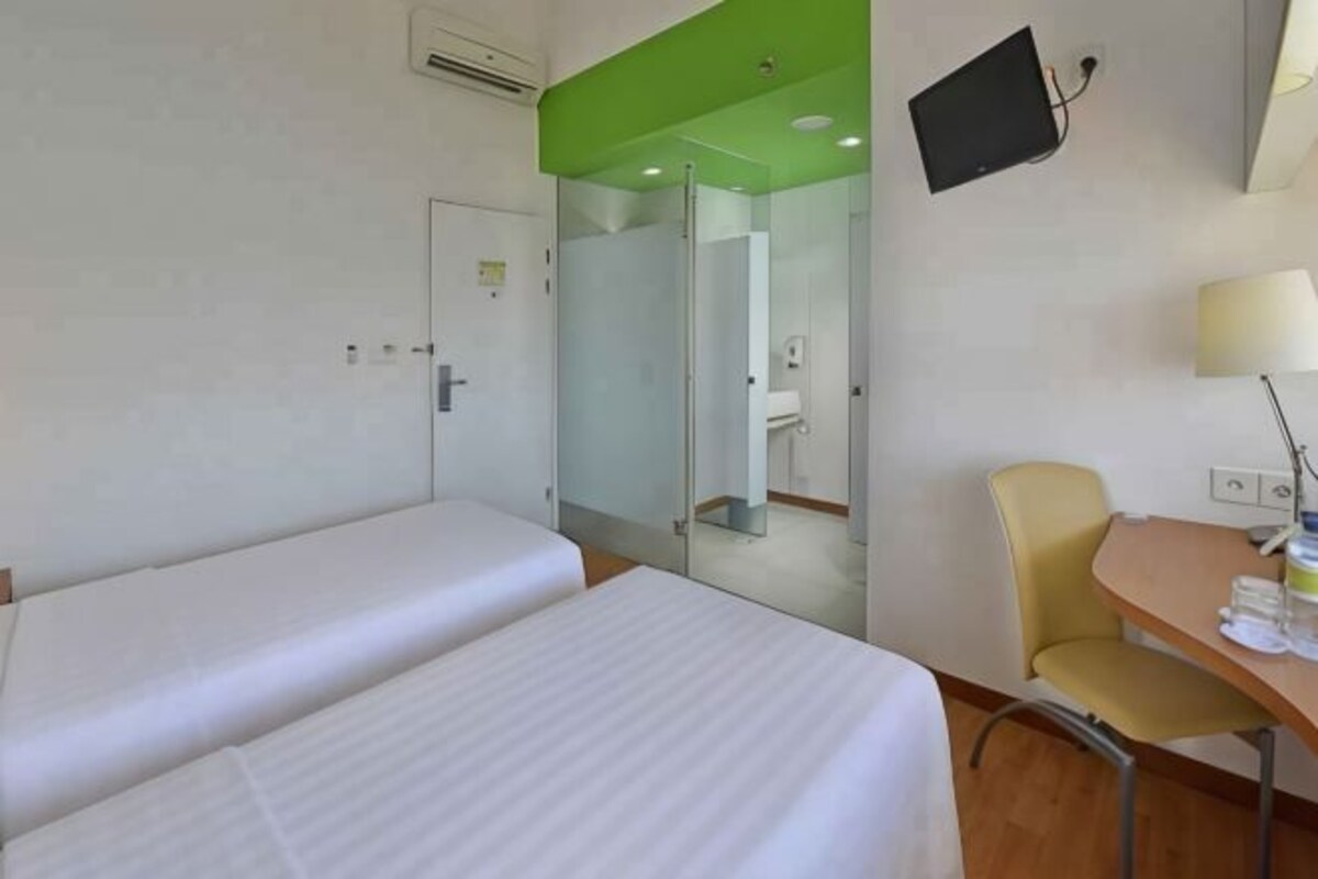 A hotel room with two beds, a desk with a chair, a television, and a mirror.