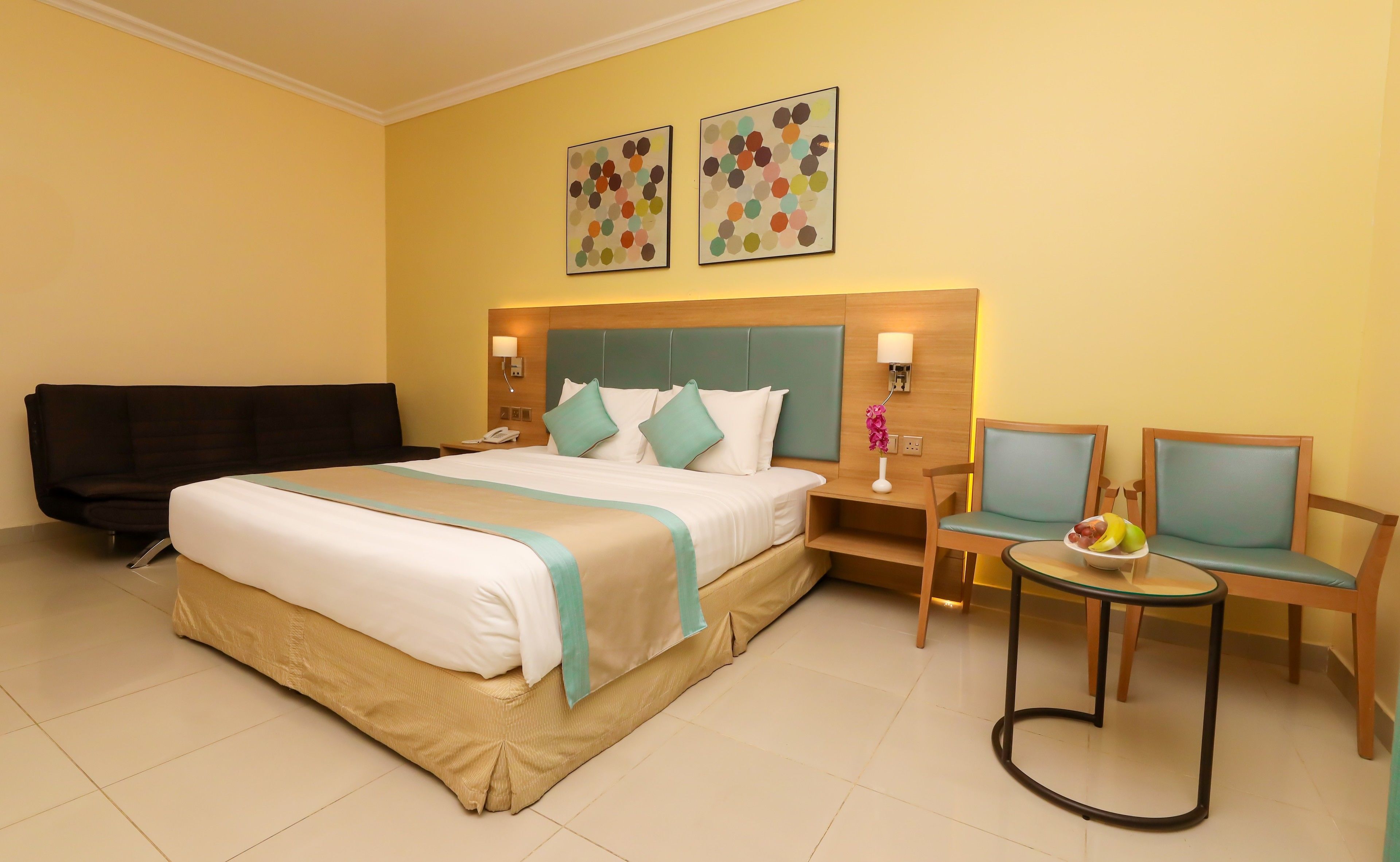 A hotel room with a large bed, two chairs, a small table, and artwork on the wall.