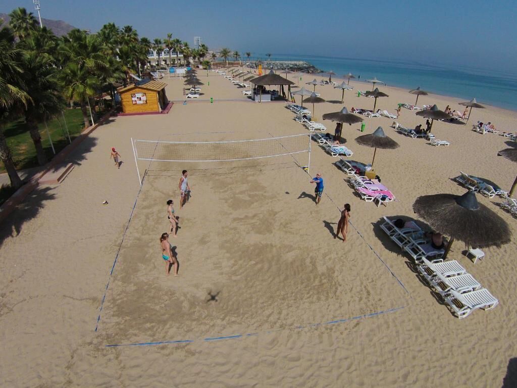 A beach volleyball court surrounded by beach umbrellas and lounge chairs.