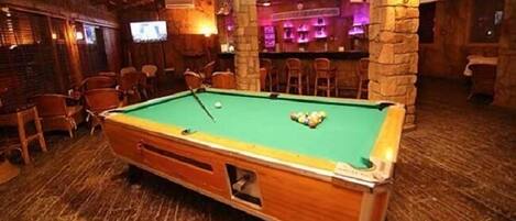 A pool table in a room with wooden flooring and stone pillars.