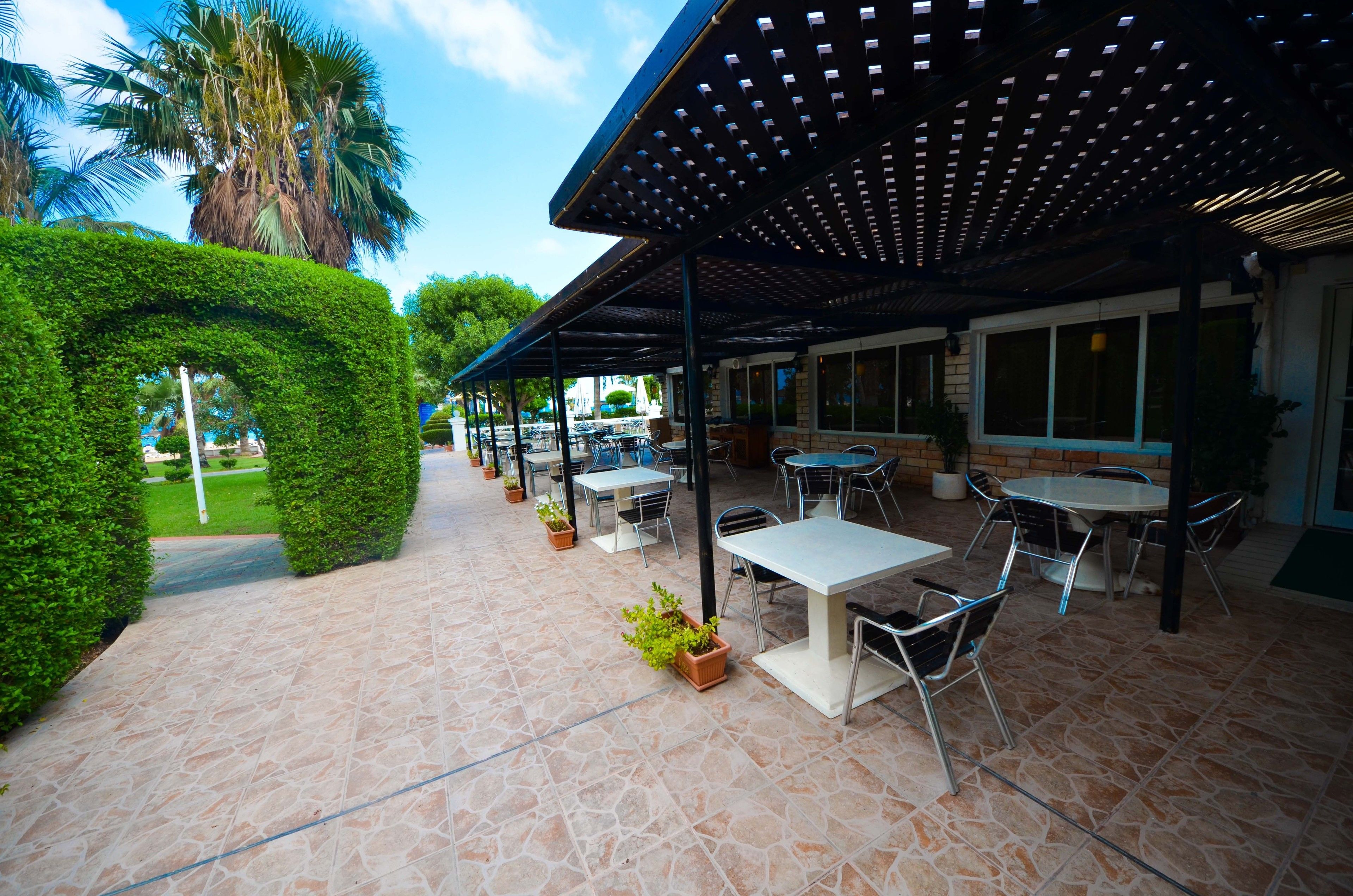 An outdoor patio area with tables and chairs, surrounded by greenery and a covered seating area.