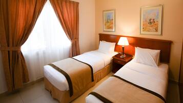 A hotel room with two beds, a nightstand with a lamp, and two paintings on the wall.