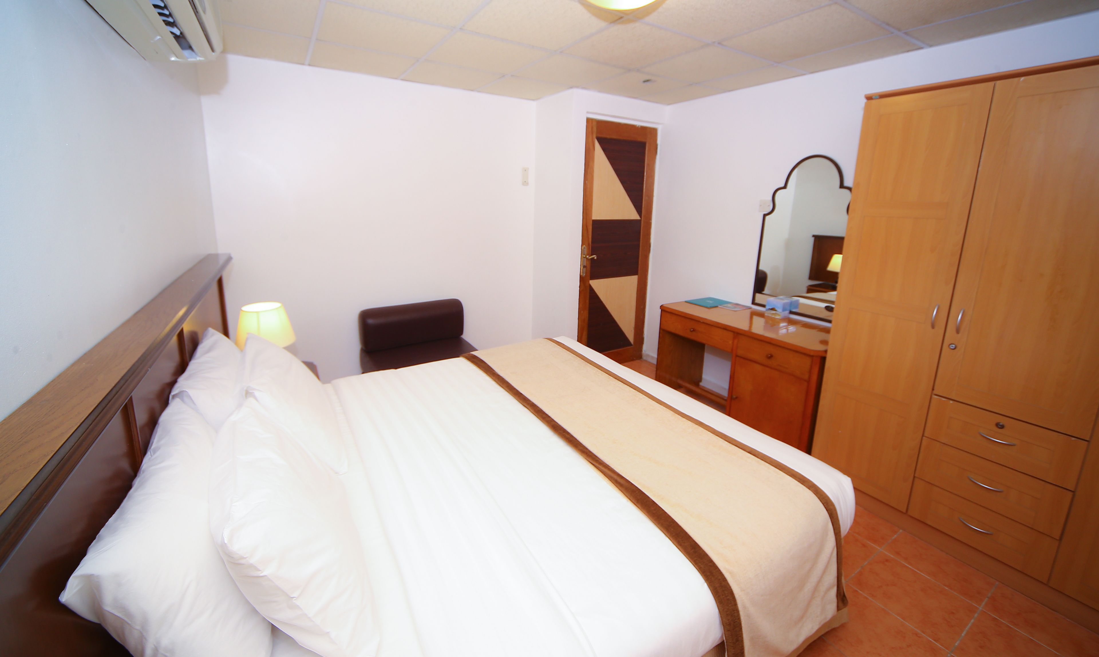 Una habitación de hotel con cama, escritorio, silla, armario y espejo.