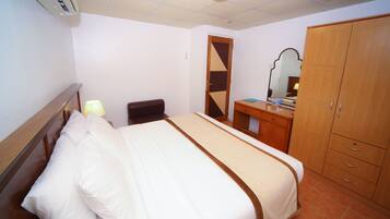 Una habitación de hotel con cama, escritorio, silla, armario y espejo.