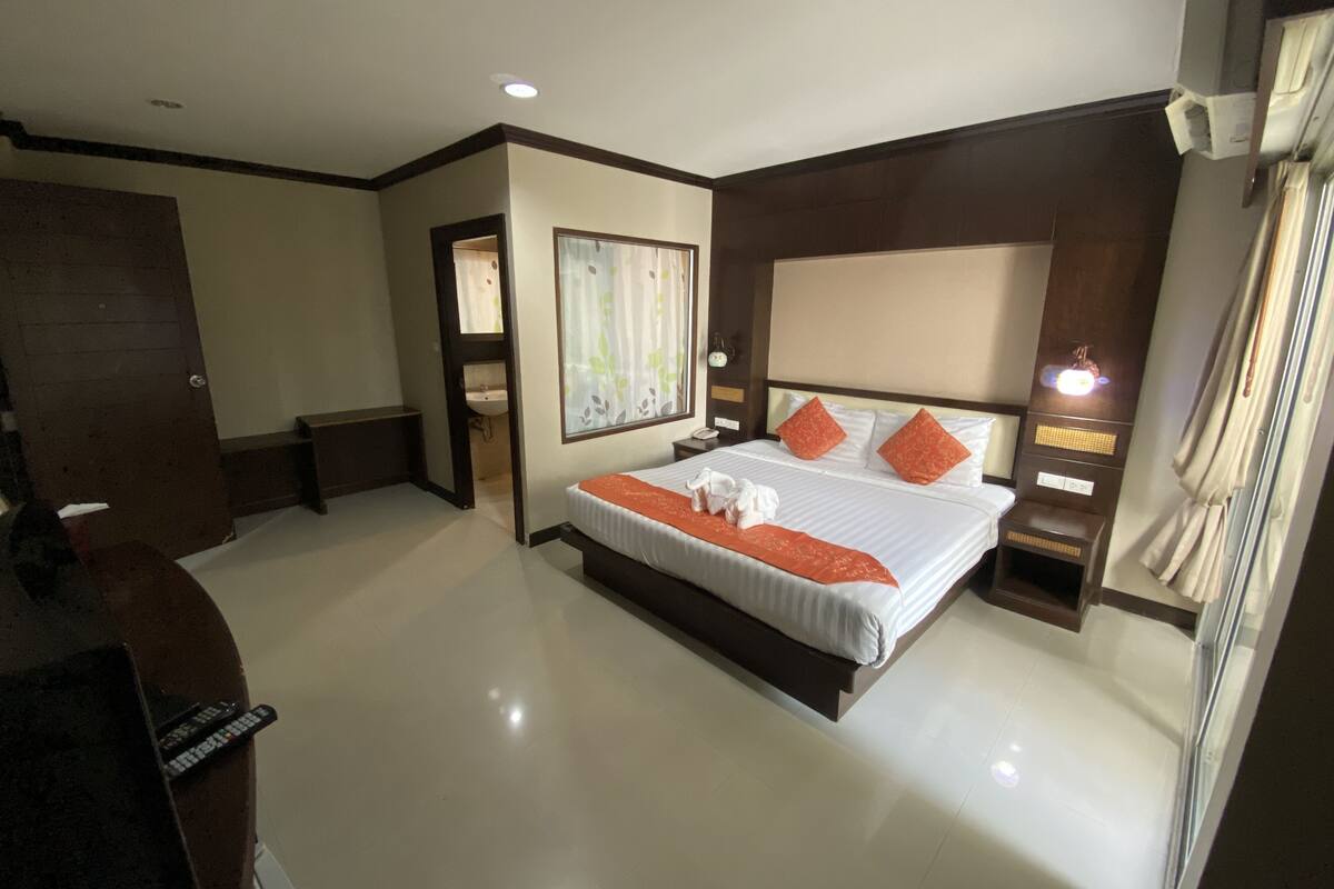 A hotel room with a large bed, bedside tables, a nightstand, a mirror, a window with curtains, and a door.