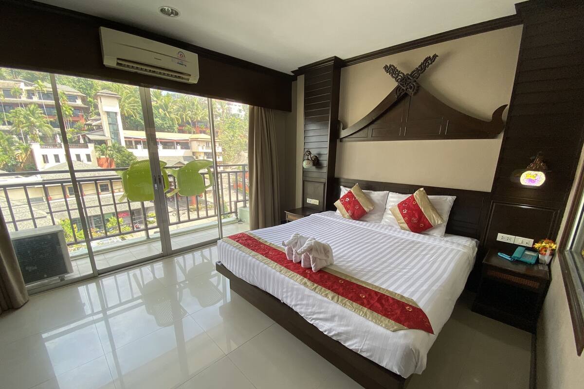 A hotel room with a large bed, a balcony with a view of buildings and palm trees, and a modern design.