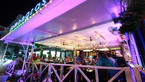 An outdoor restaurant with a neon sign, white railings, and indoor seating. - Lemongrass Hotel (Patong)