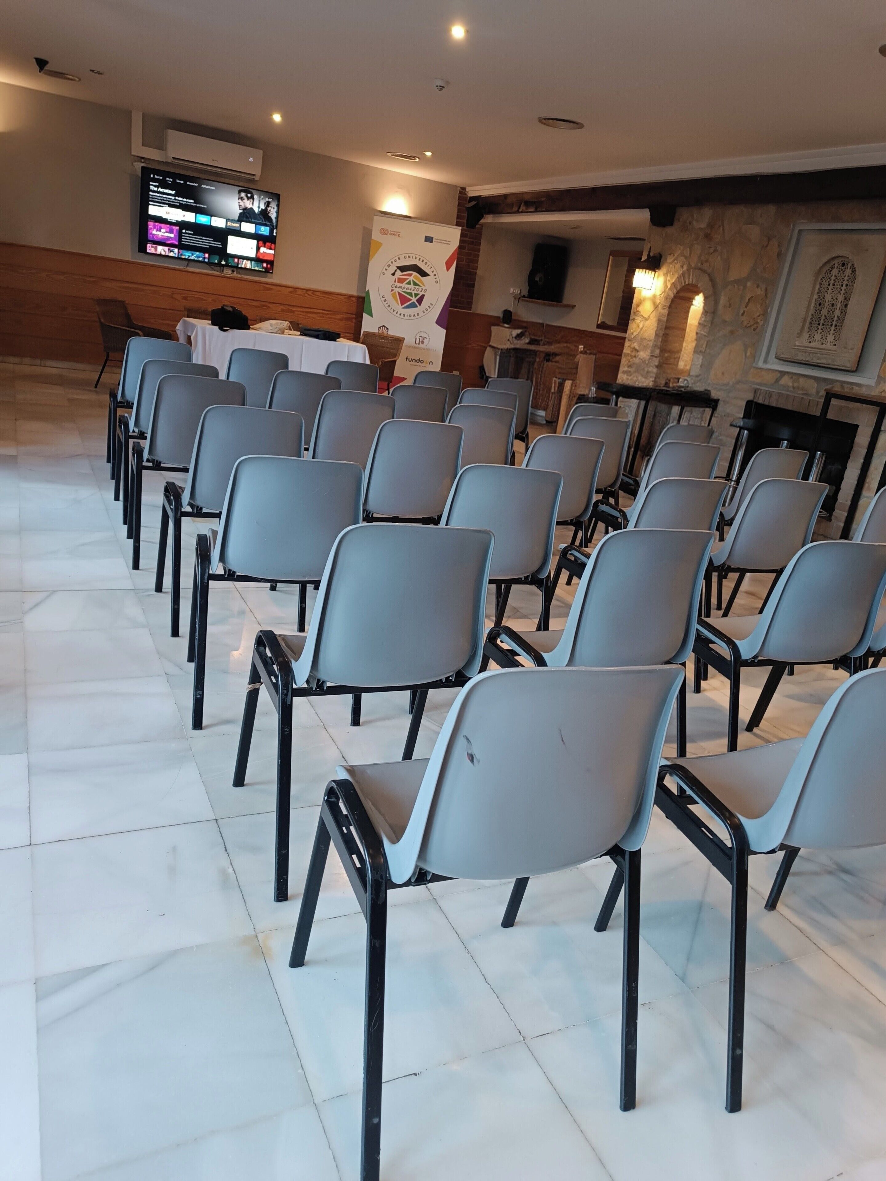 A conference room with rows of chairs, a television screen, and a stone wall with a fireplace.