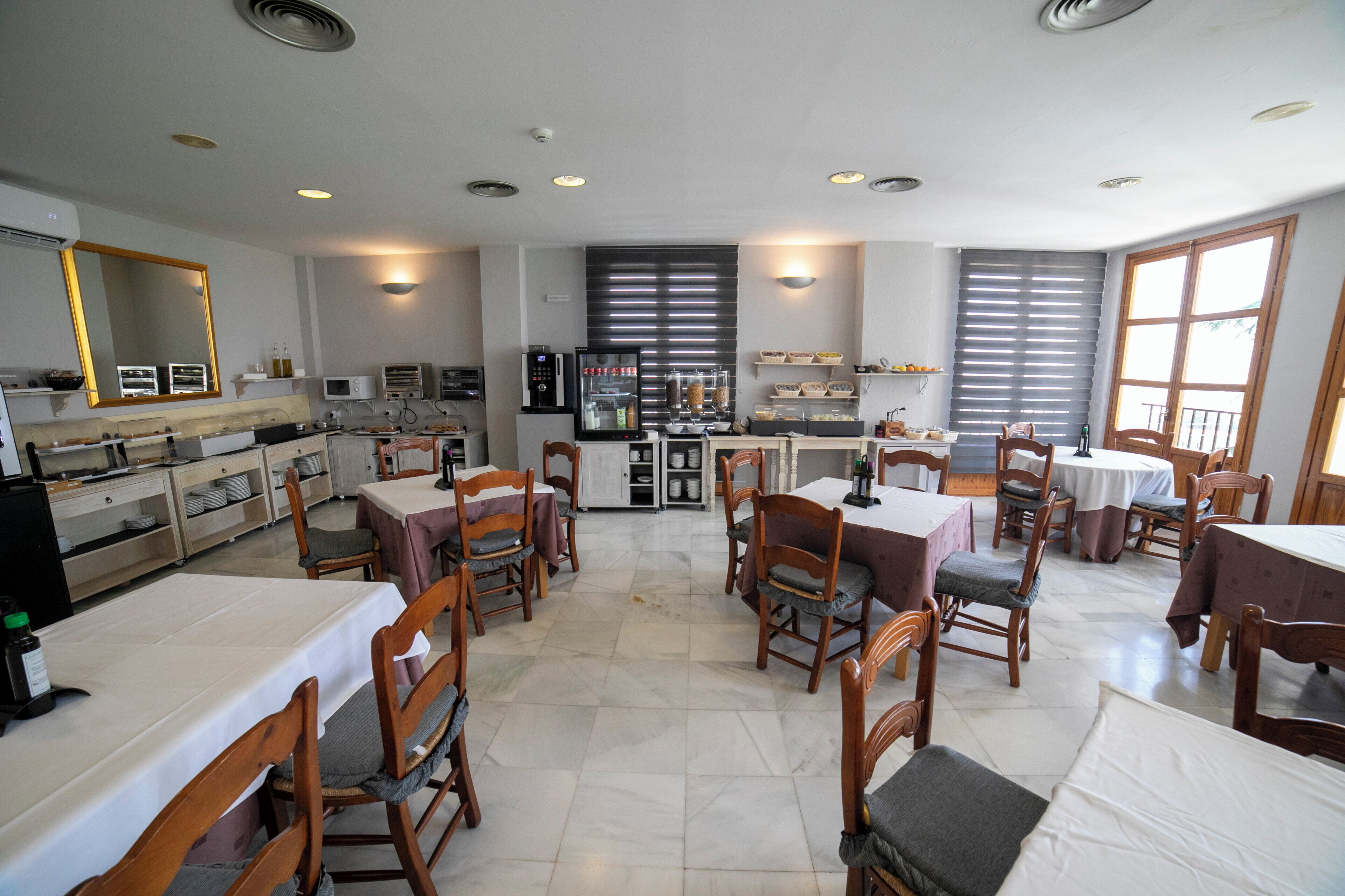 A spacious dining area with multiple tables and chairs, a kitchen area with appliances, and a large mirror on the wall.