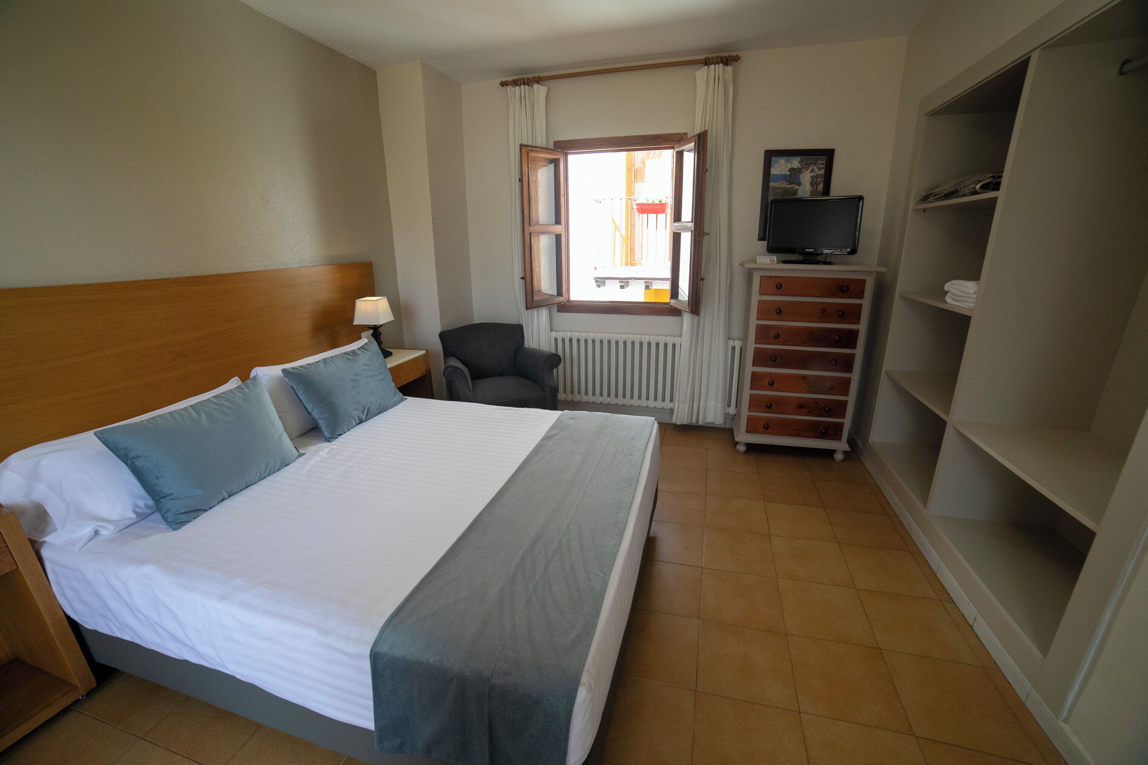 A hotel room with a large bed, a chair, a TV on a stand, and a wardrobe.