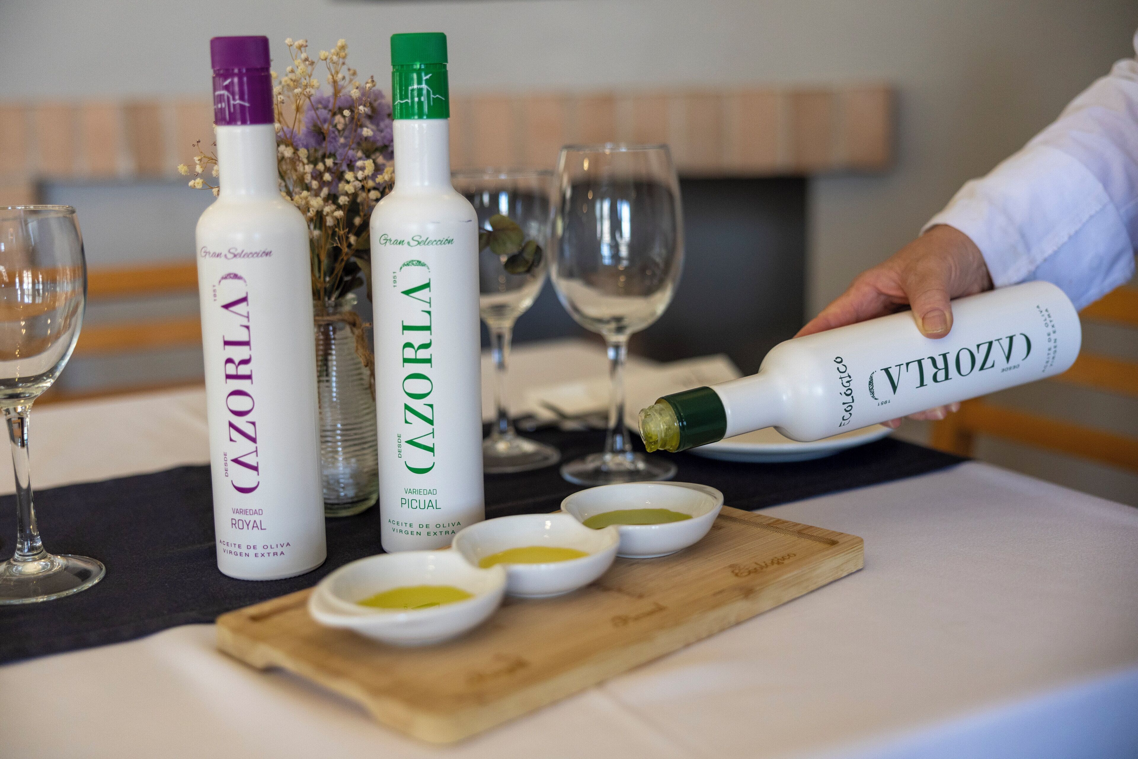 Una mesa con botellas de vino Cazorla, recipientes pequeños de aceite de oliva y copas de vino.