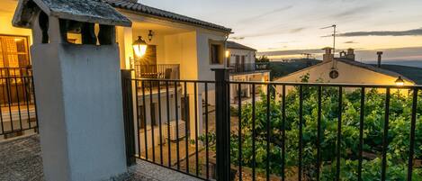 A villa with a balcony, a stone wall, and a view of a vineyard.