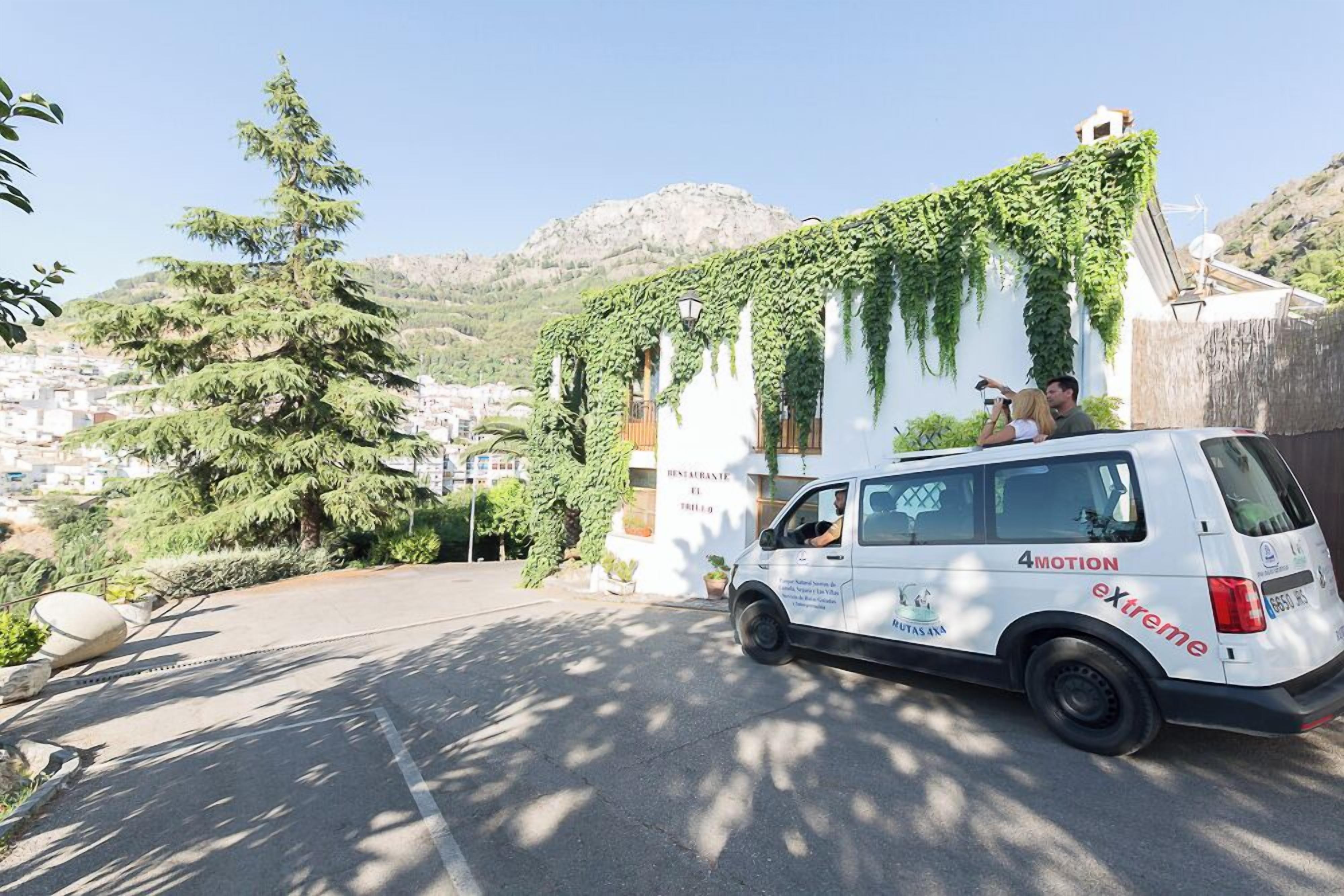 A white van parked in front of a building with ivy-covered walls, a clear sky, and a mountainous backdrop.