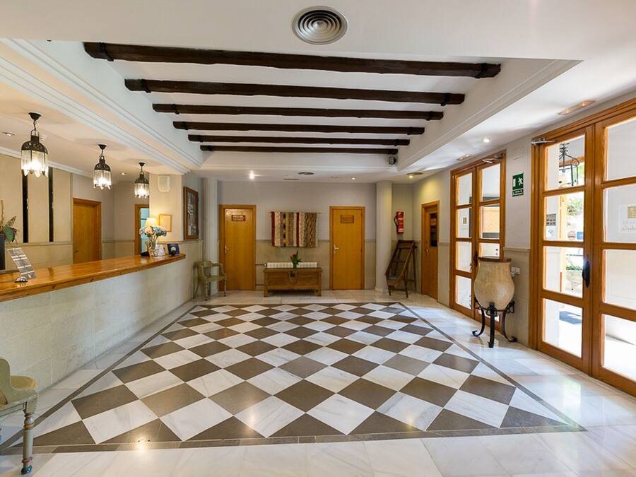 Un vestíbulo de hotel con piso a cuadros, vigas de madera en el techo, una recepción y ventanas amplias.