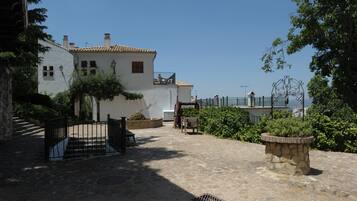 A courtyard with a stone floor, a white building with a tiled roof, and a metal gate.