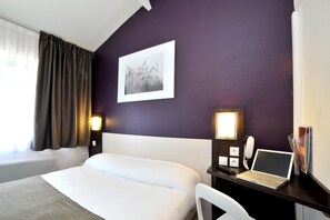 A hotel room with a bed, a desk with a laptop, a telephone, and a wall-mounted picture. - Brit Hotel Confort Lyon Dardilly (Dardilly)