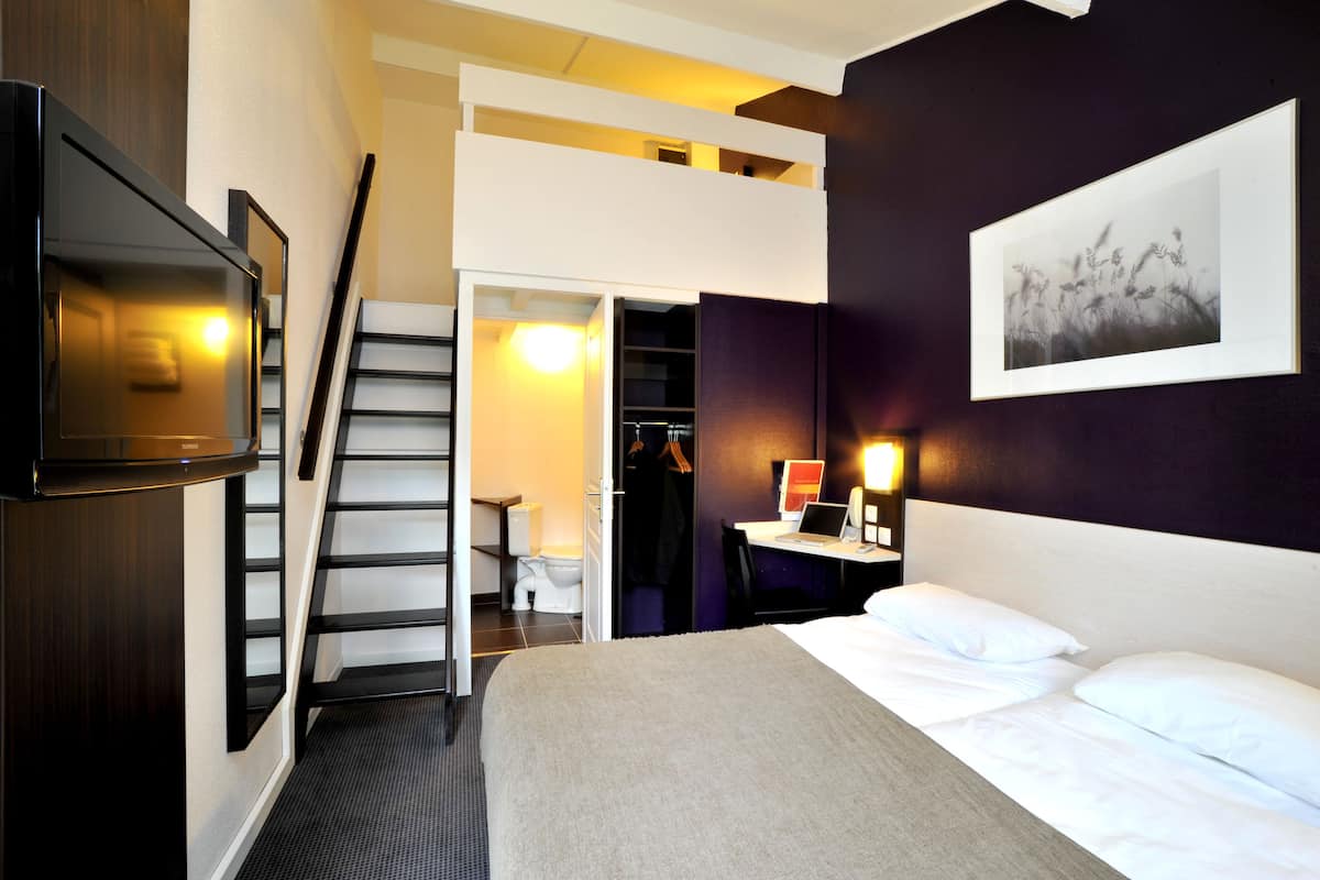 A hotel room with a bed, a desk with a laptop, a TV, a wardrobe, and a staircase.