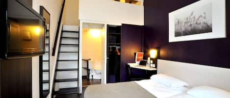 A hotel room with a bed, a desk with a laptop, a TV, a wardrobe, and a staircase.