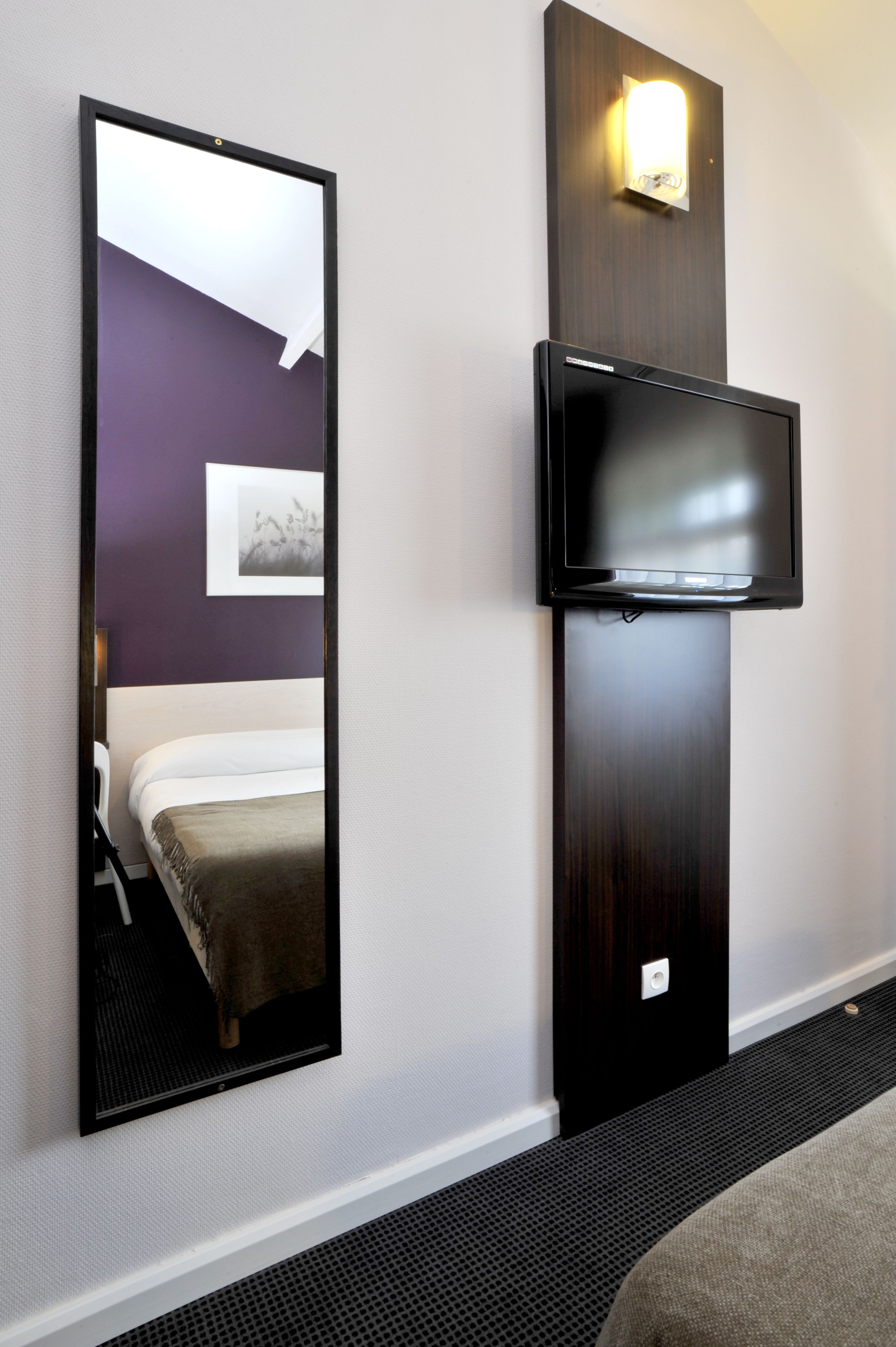 Een hotelkamer met een bed, een televisie aan de muur en een grote spiegel.