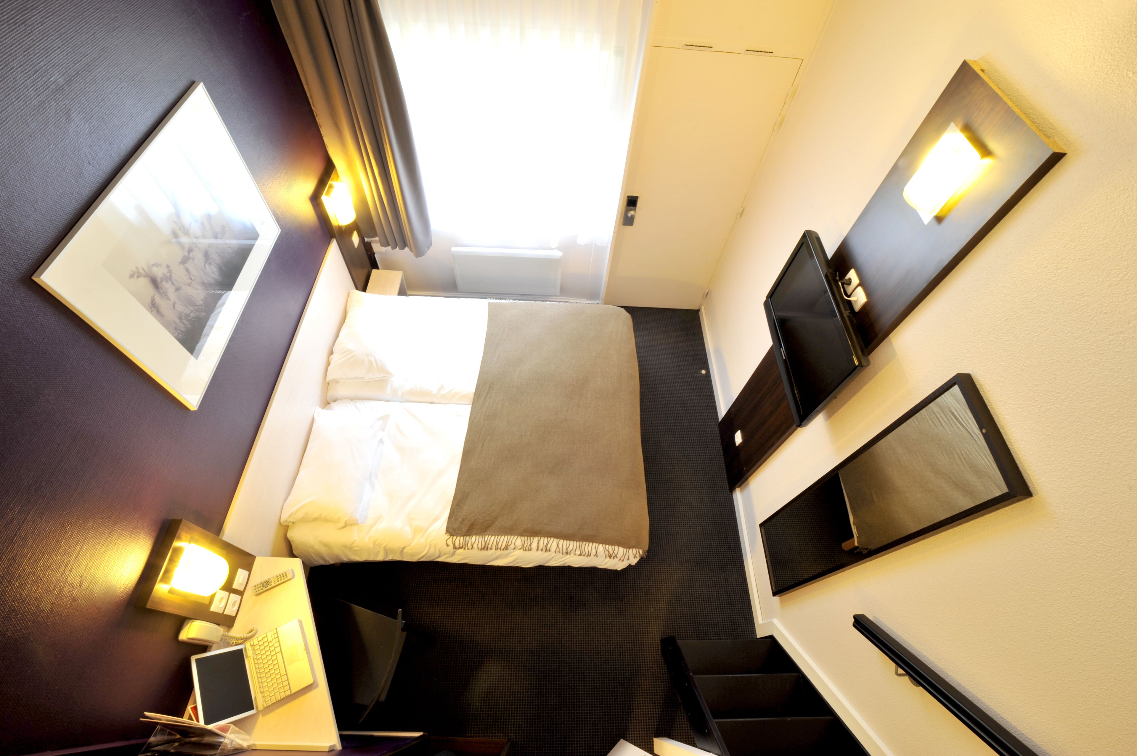 Habitación de hotel con cama, mesitas de noche, un escritorio con una computadora portátil, una silla, un televisor y una ventana con cortinas.