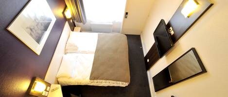 Habitación de hotel con cama, mesitas de noche, un escritorio con una computadora portátil, una silla, un televisor y una ventana con cortinas.