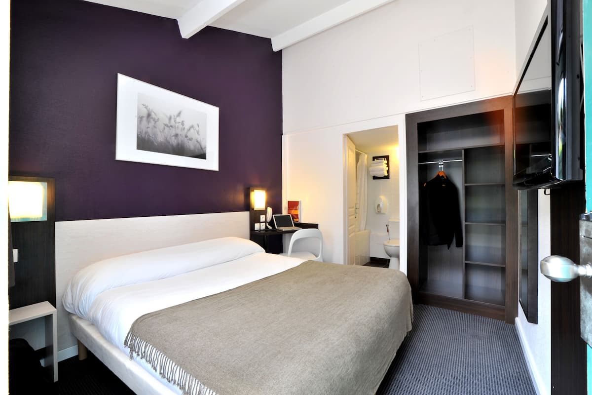 A hotel room with a bed, a desk with a laptop, a coat rack, and a walk-in closet.